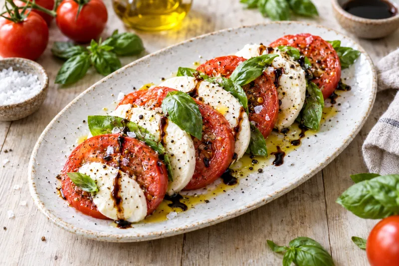 Vegane Insalata Caprese auf weißem Teller mit Tomaten, veganer Mozzarella, Basilikum und Balsamico-Reduktion