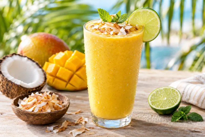 Veganer Mango-Kokos-Smoothie in Gläsern mit Kokosraspeln und Limettenscheibe