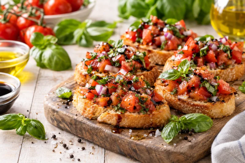 Vegane Bruschetta auf Holzbrett mit Tomatenwürfeln und Basilikum
