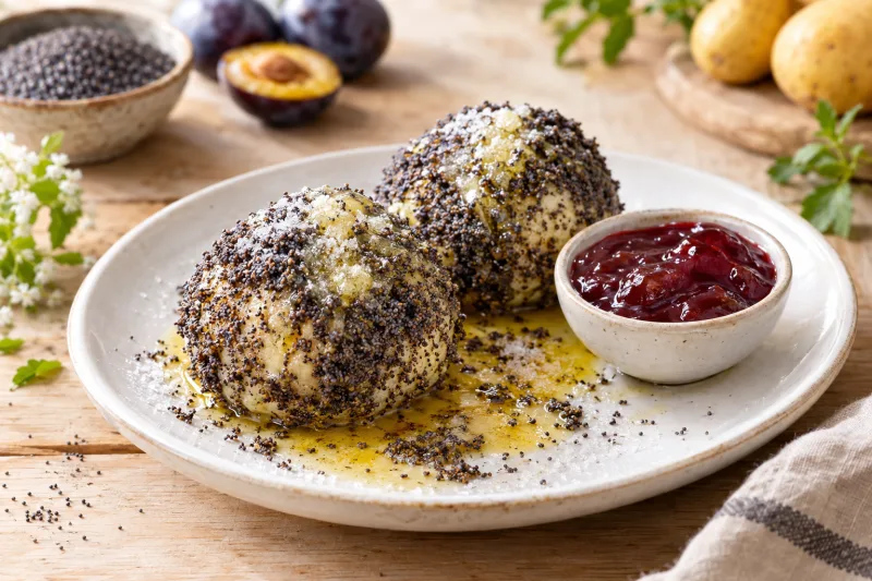 Vegane Mohnklöße auf einem Teller, mit Mohn bestreut und flüssiger veganer Butter übergossen