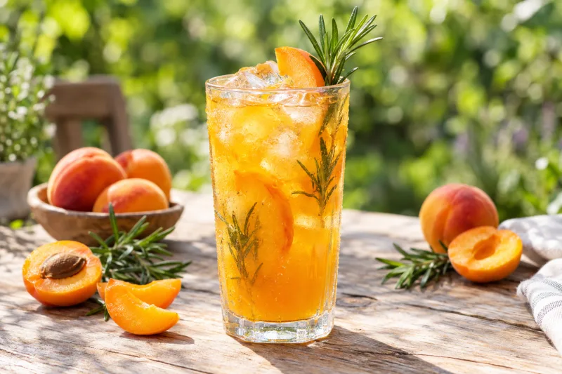 Glas mit Aprikosen-Rosmarin Eistee, Eiswürfeln und frischer Minze