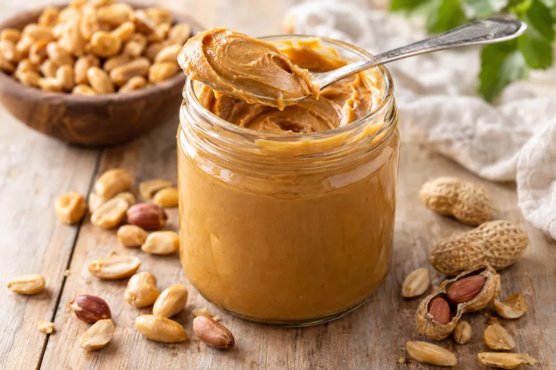 Cremige vegane Erdnussbutter in einem Glas, mit Erdnüssen und Löffel