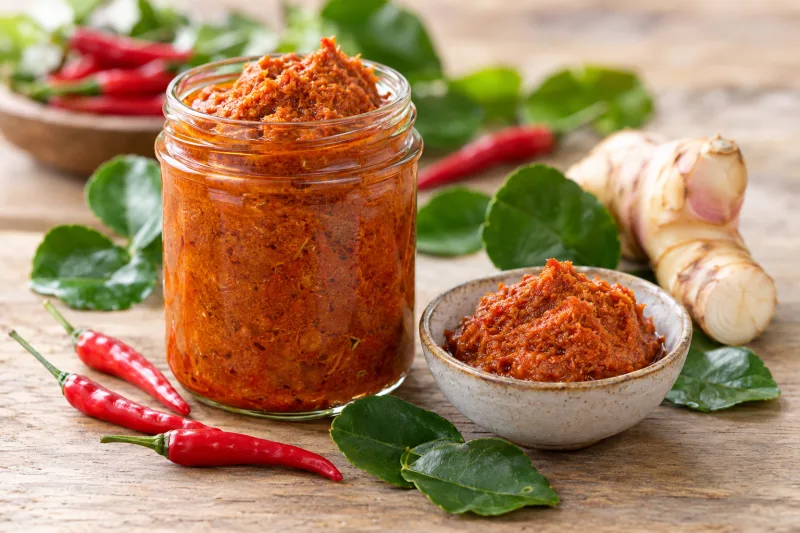 Vegane Gulai Currypaste in einem Glas mit frischen Chilis und Limettenblättern