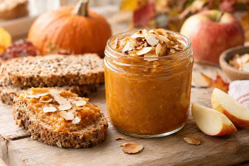 Veganer Kürbis-Apfel-Aufstrich in einem Glas, bestreut mit Mandelblättchen, daneben frisches Brot.