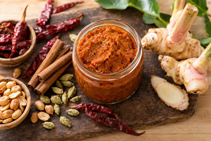 Vegane Massaman Currypaste in einem Glas mit Erdnüssen und Gewürzen daneben