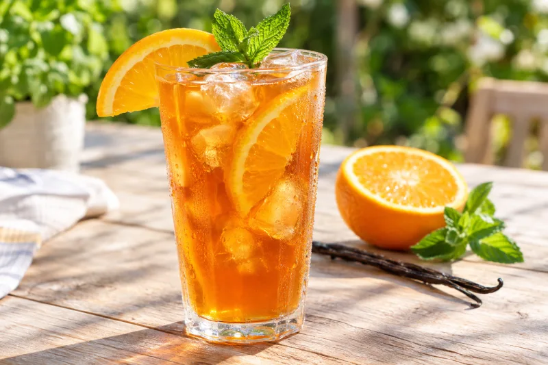 Glas mit veganem Orangen-Vanille-Eistee, garniert mit Orangenscheibe und Minze
