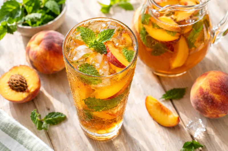 Glas mit eiskaltem Pfirsich-Eistee, Pfirsichspalten, Minze und Eiswürfeln