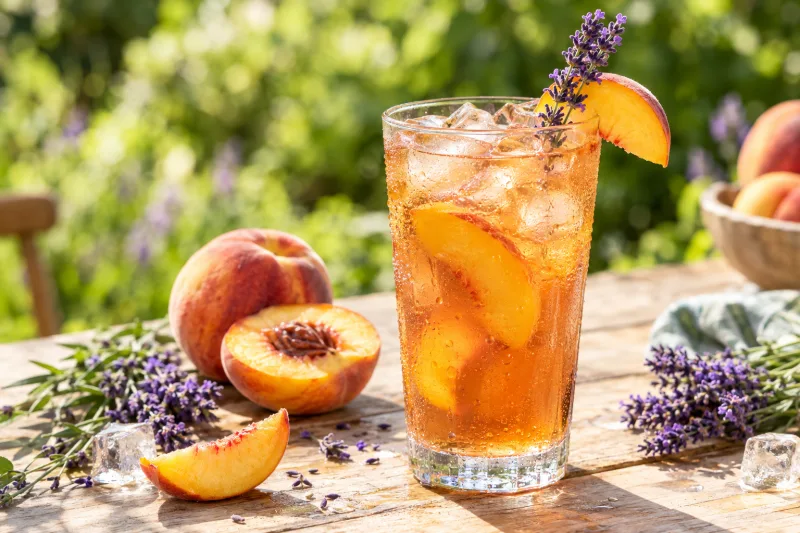 Glas mit Pfirsich-Lavendel Eistee, Eiswürfeln, Pfirsichscheibe und Lavendelzweig