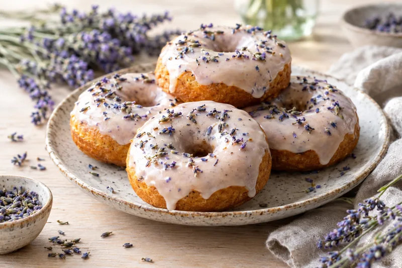 Goldbraune vegane Vanille-Lavendel-Donuts mit weißer Glasur und Lavendelblüten auf einem Teller