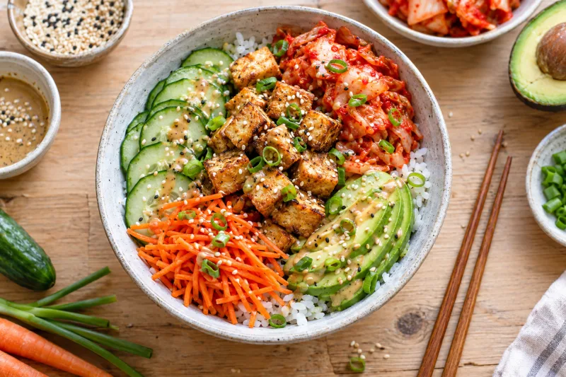 Vegane Kimchi-Bowl mit Tofu, Avocado, Karotten, Gurke und Sesam in einer hellen Schüssel