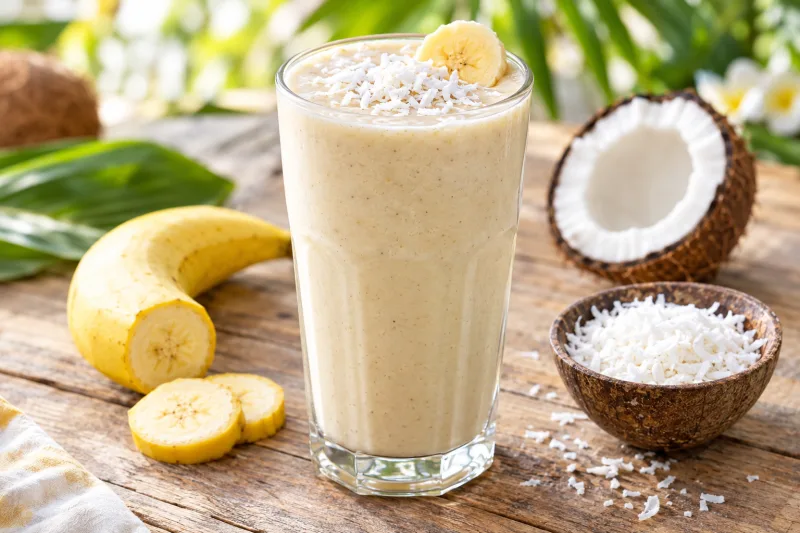 Cremiger veganer Bananen-Kokosnuss-Smoothie in einem Glas mit Kokosraspeln garniert