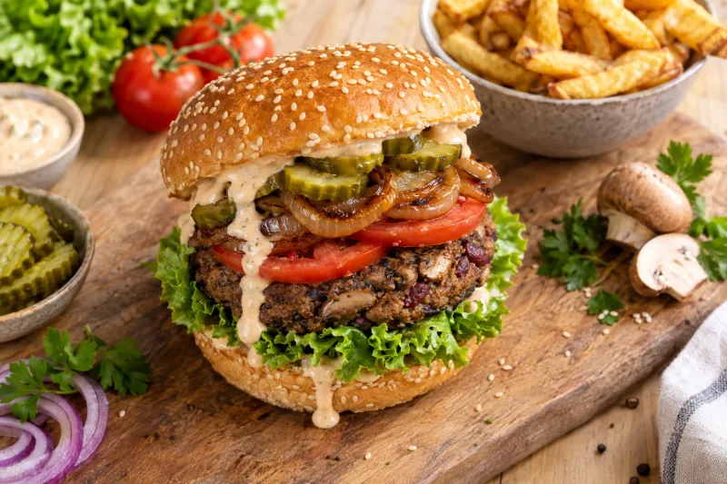 Veganer Pilz-Burger mit Salat, Tomaten und Sauce auf einem Holzbrett