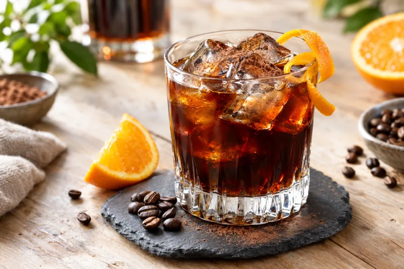 Veganer Black Russian Cocktail im Glas mit Eiswürfeln und Orangenzeste