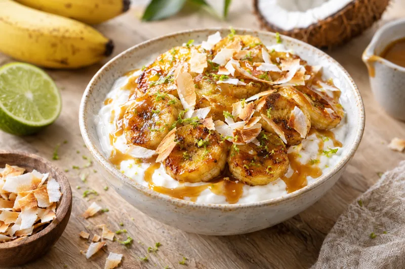 Karamellisierte Bananen mit Kokosjoghurt in einer Schale mit Kokosraspeln bestreut